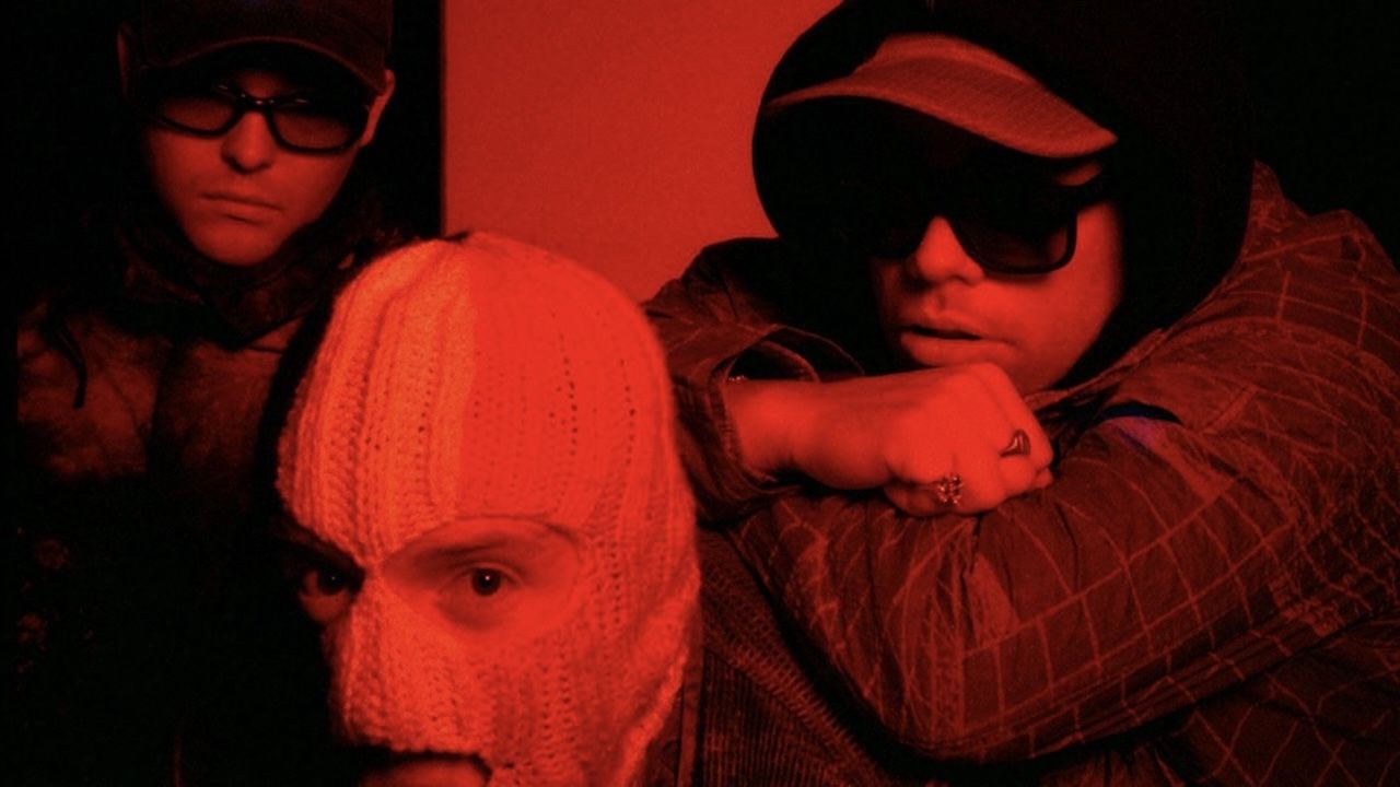 “Ya think it’s all poetry and clovers, when it’s raincoats and police Land Rovers. Salt of the earth, looking over their shoulder.” Kneecap share moody and intense new single Smugglers & Scholars